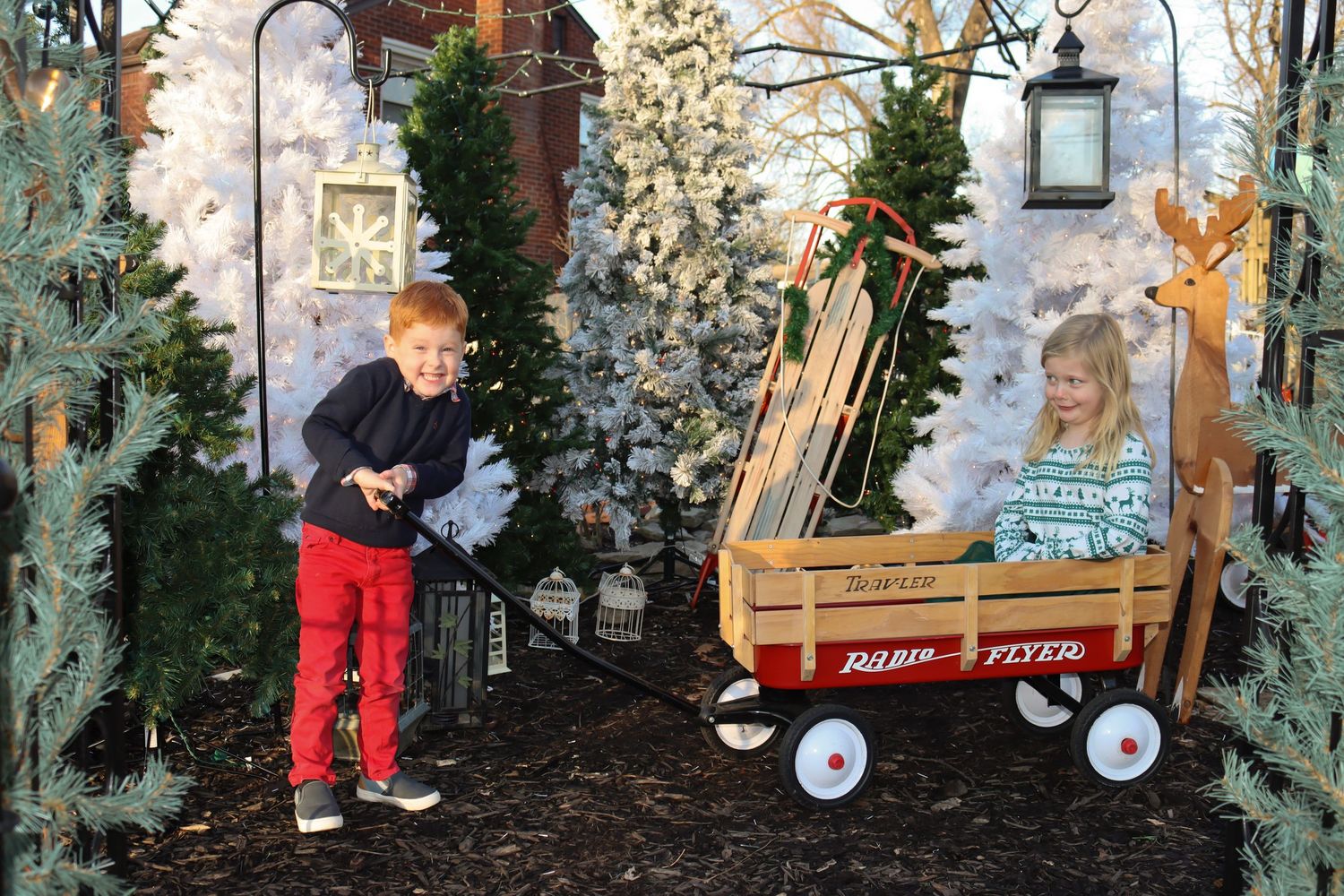 A holiday display featuring a red Radio Flyer wagon surrounded by decorated Christmas trees.