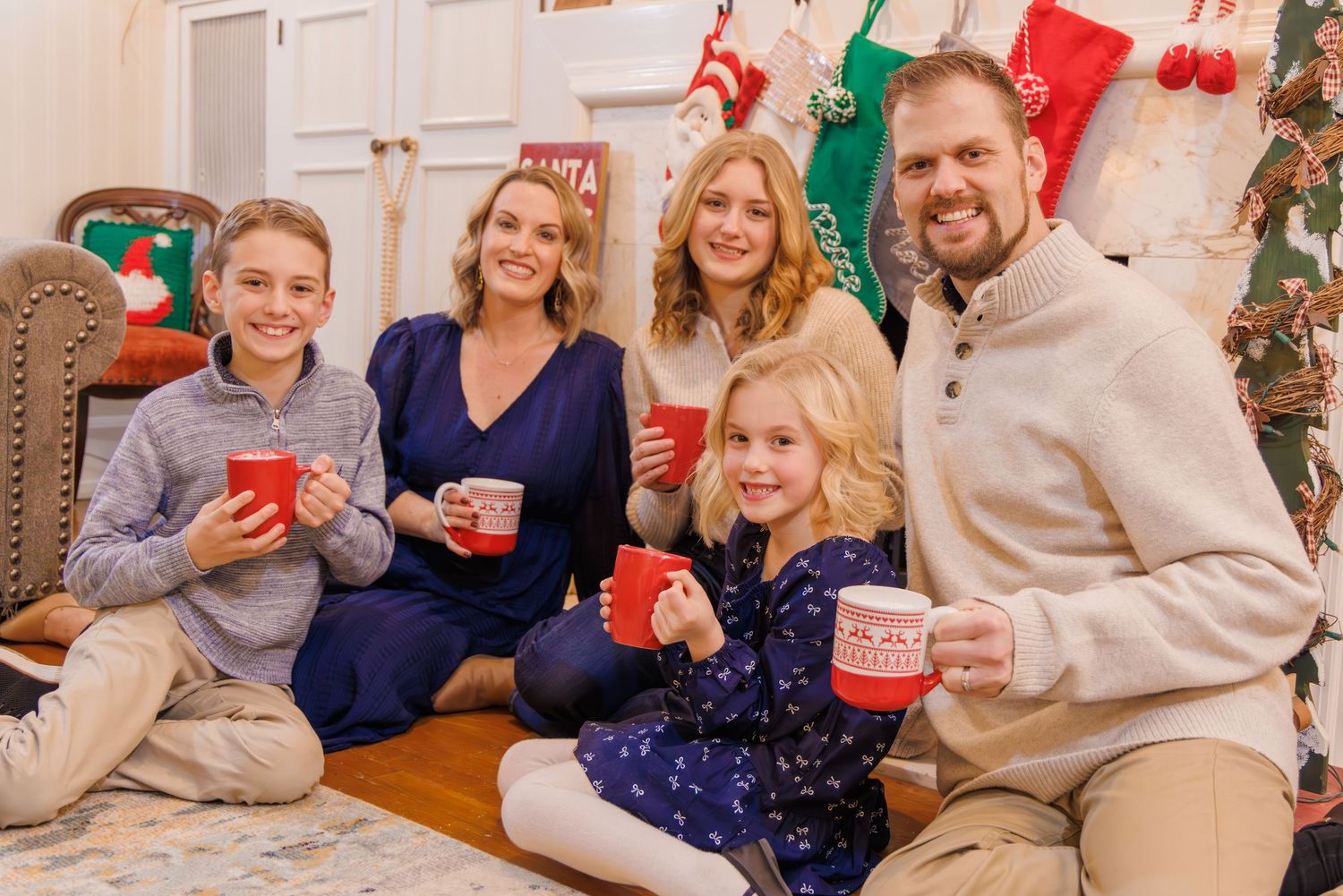 Family gathering in a living room decorated for Christmas with festive sweaters and holiday decor.