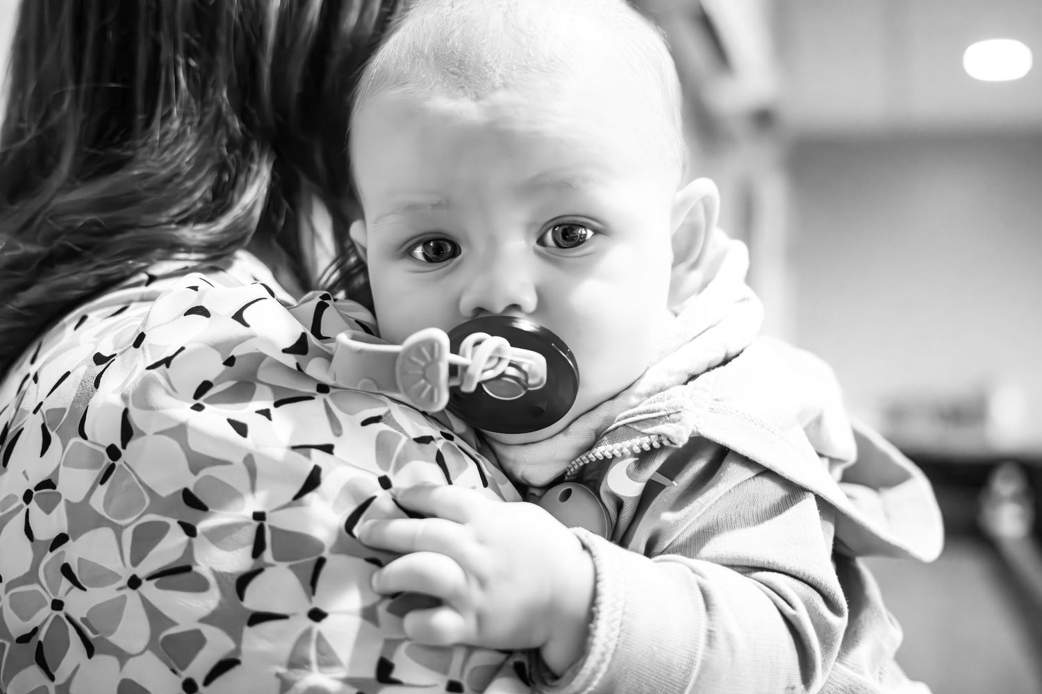 Black and white photo of an infant with a pacifier being held.