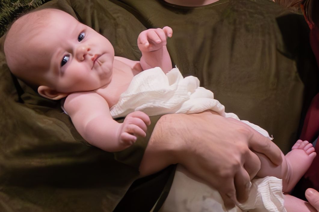 An infant in white clothing lying on someone's lap.