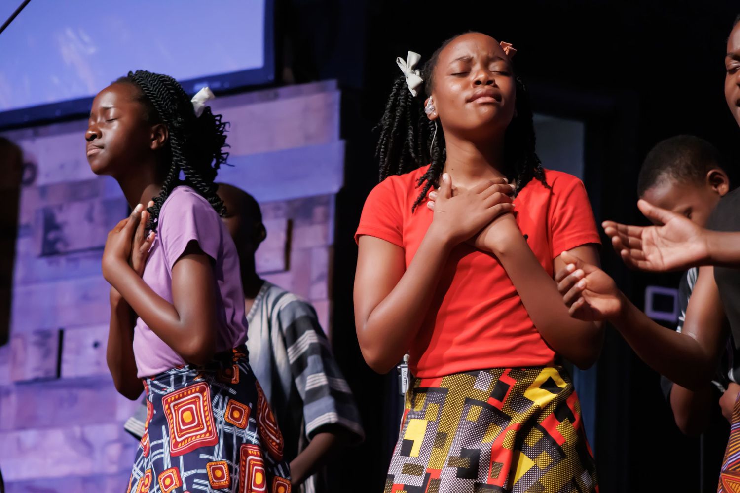 Performers in colorful outfits singing with expressive gestures on stage.