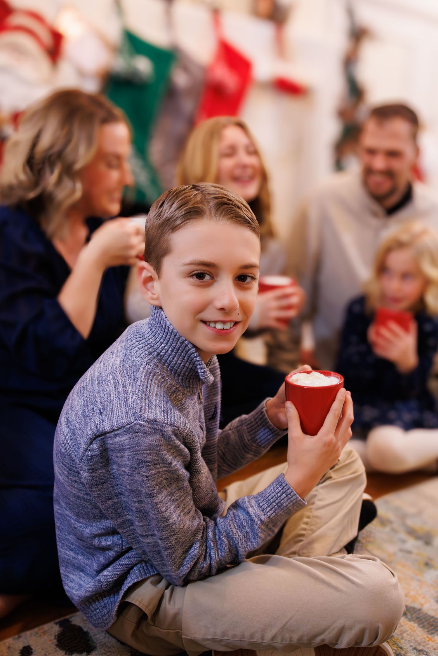 Child in grey sweater enjoying hot cocoa during holiday celebration.