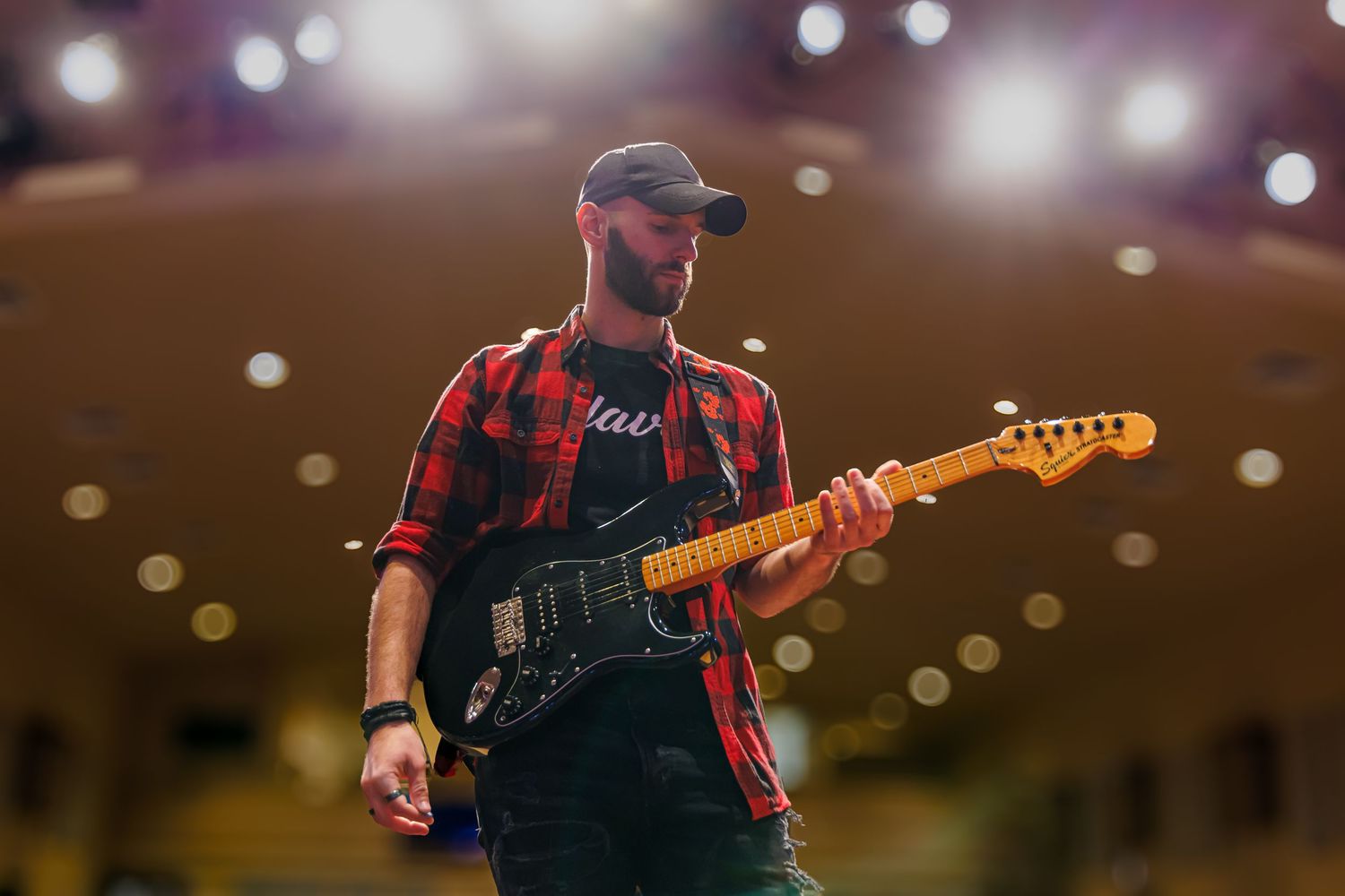 Close-up of guitar player performing on stage with colorful bokeh lights in the background.