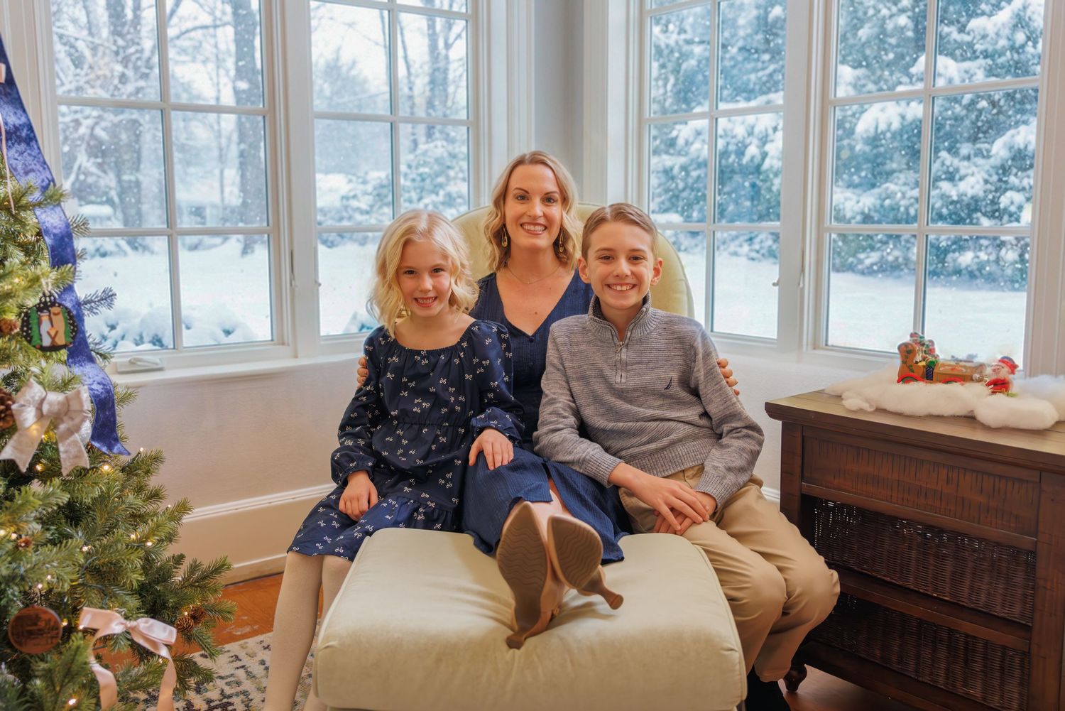 Family sitting together on window bench with winter scene visible outside.