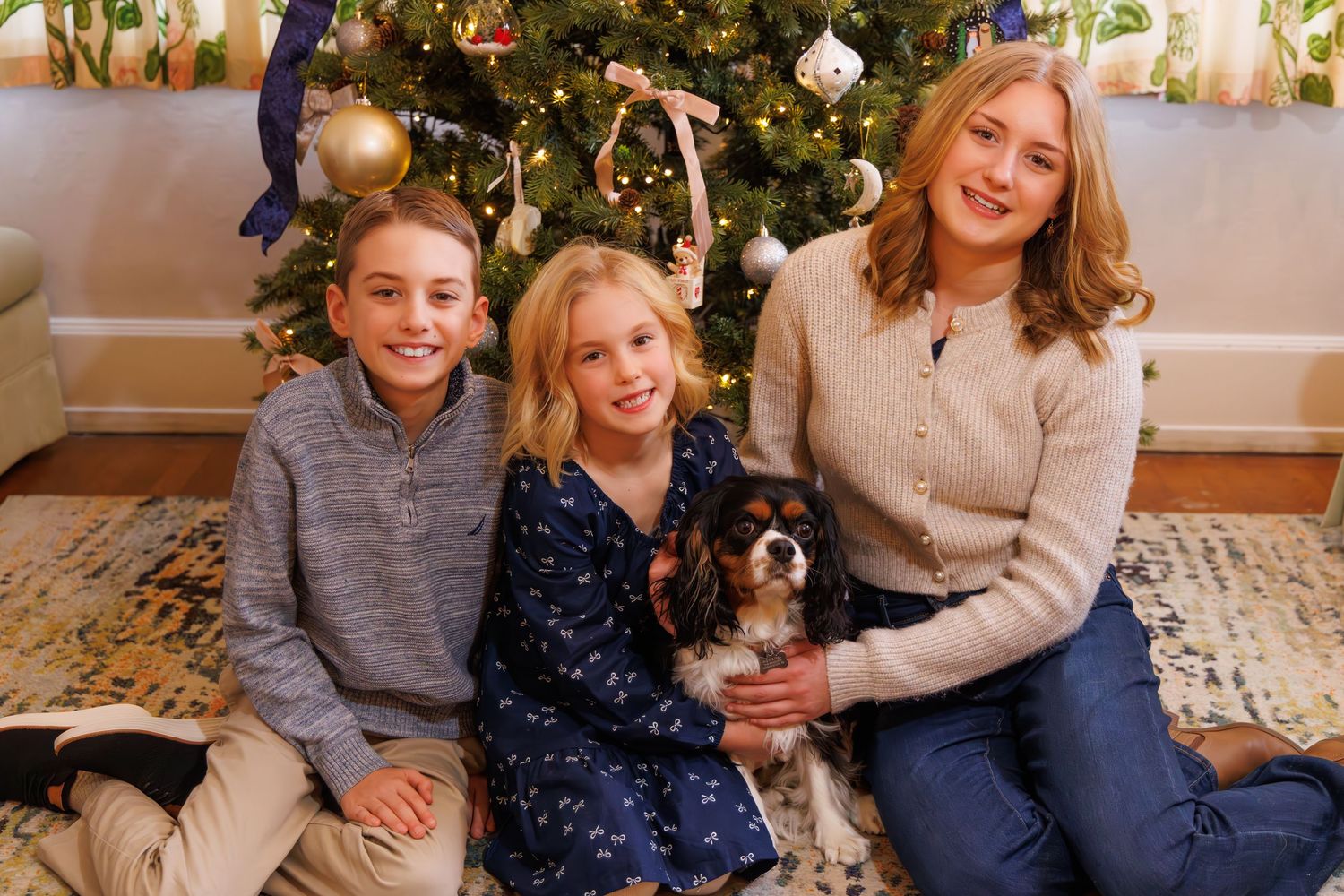 Cozy family Christmas scene with decorated tree and people sitting together on floor.
