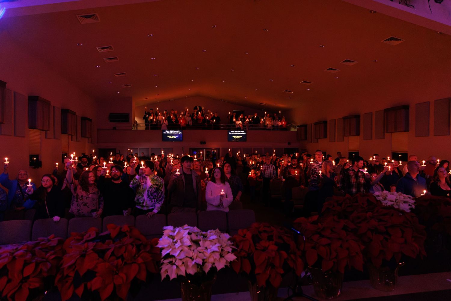A crowded concert hall illuminated with dramatic red and purple lighting during a performance.