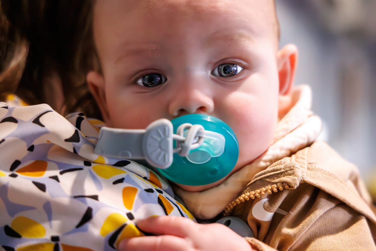 Close up of a baby with bright eyes using a teal pacifier.