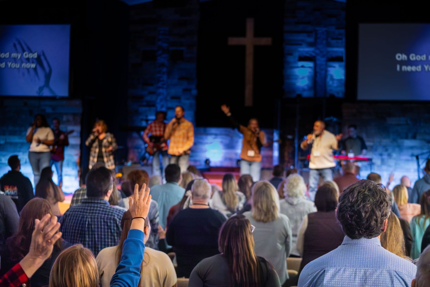Church worship service with raised hands and cross illuminated in blue light.