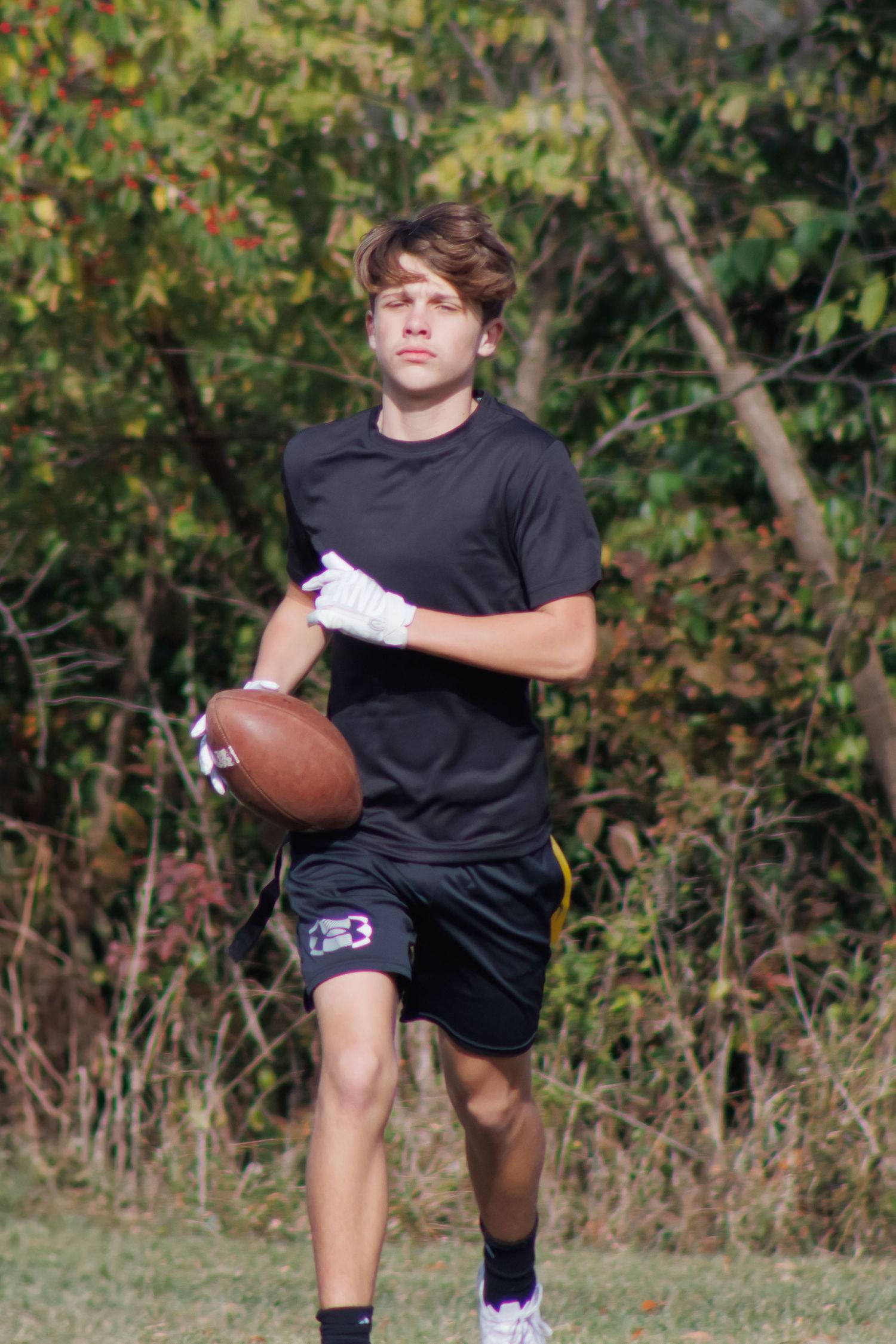 A flag football player in black athletic wear practicing with a football outdoors.