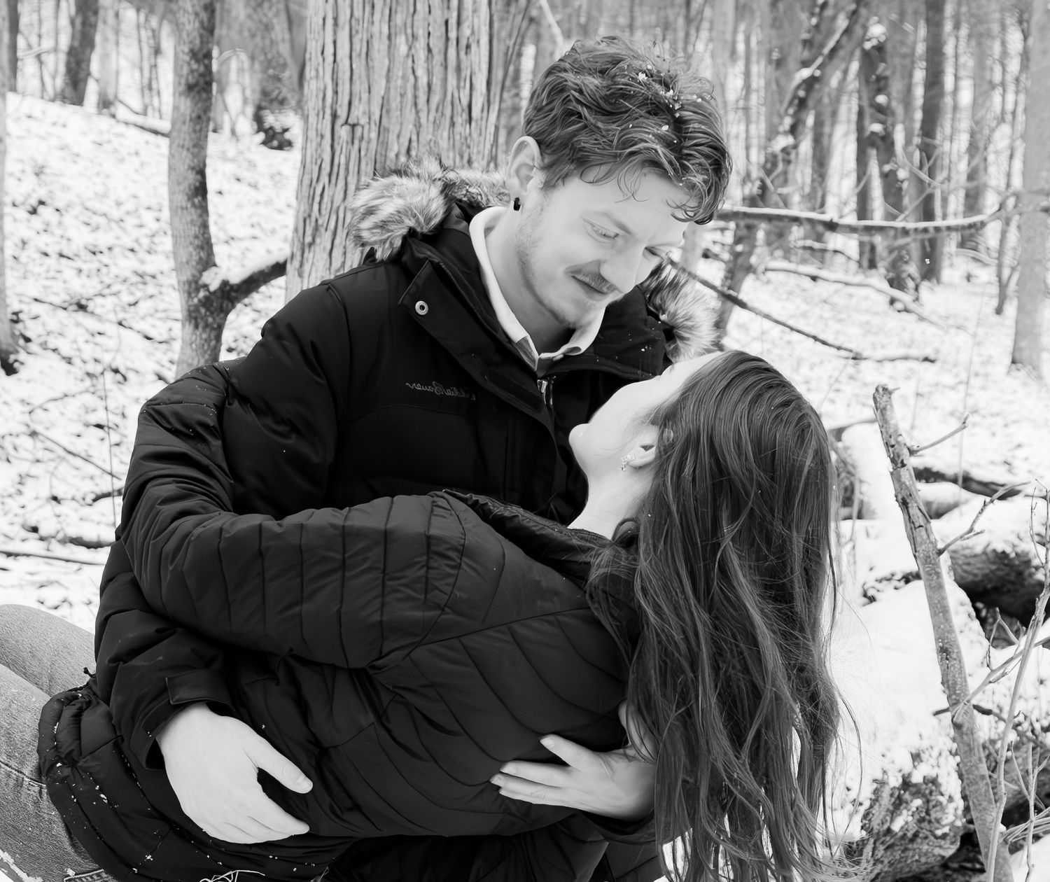 A couple shares an intimate moment in a snow-covered forest setting.