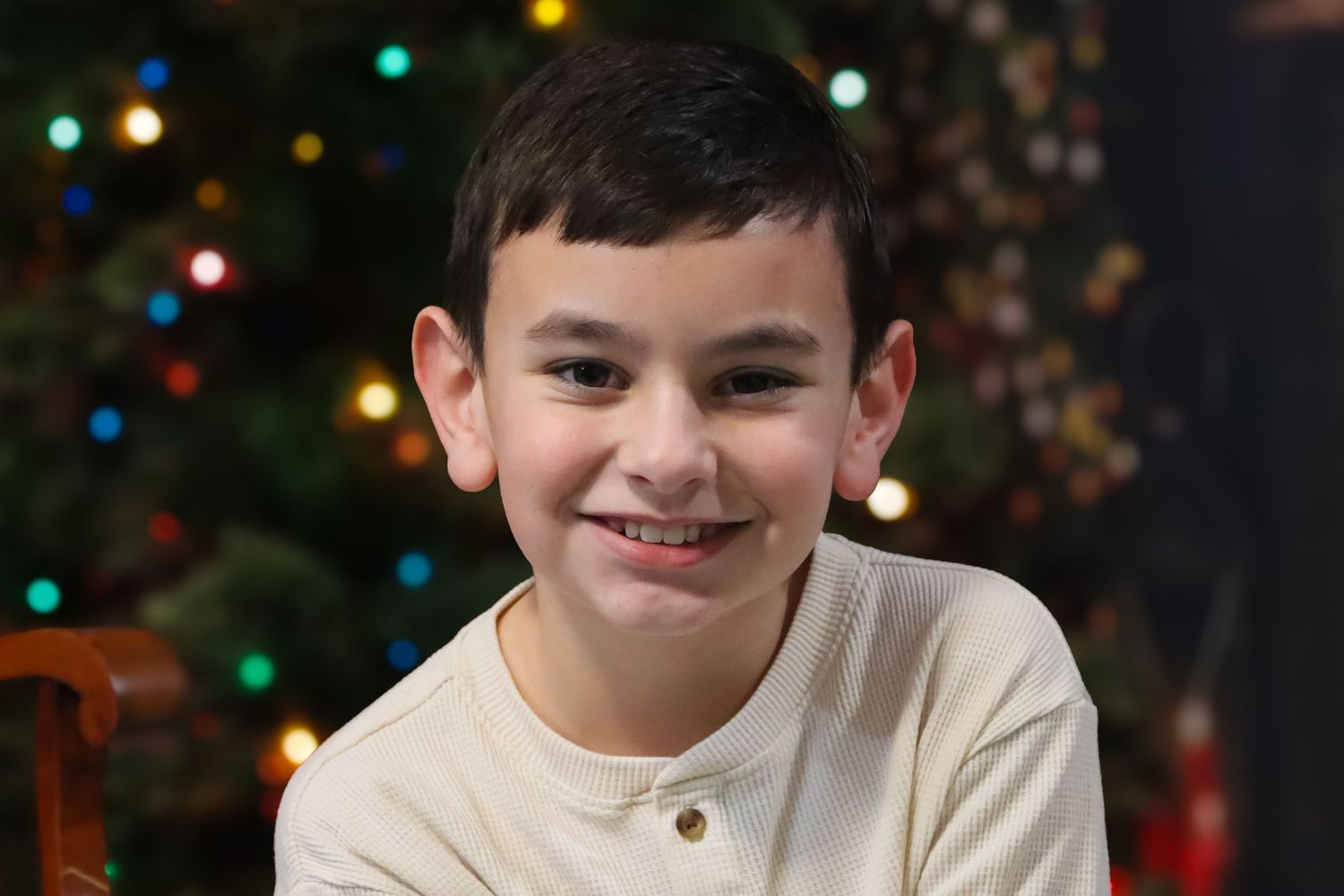 Holiday portrait session with decorated Christmas tree and colorful lights in background.