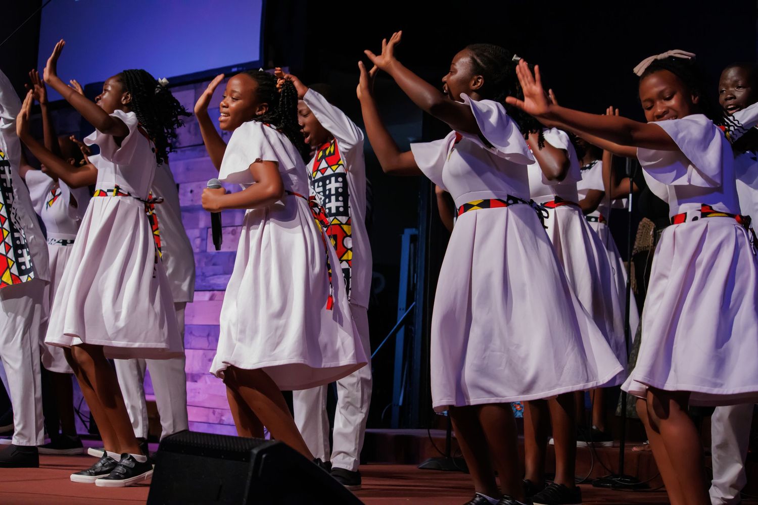 Gospel choir in white dresses performing with synchronized arm movements.