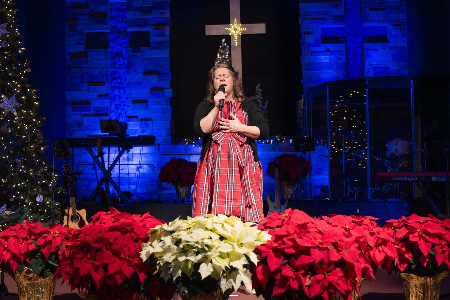 A festive church stage decorated with poinsettias, Christmas trees, and twinkling lights.