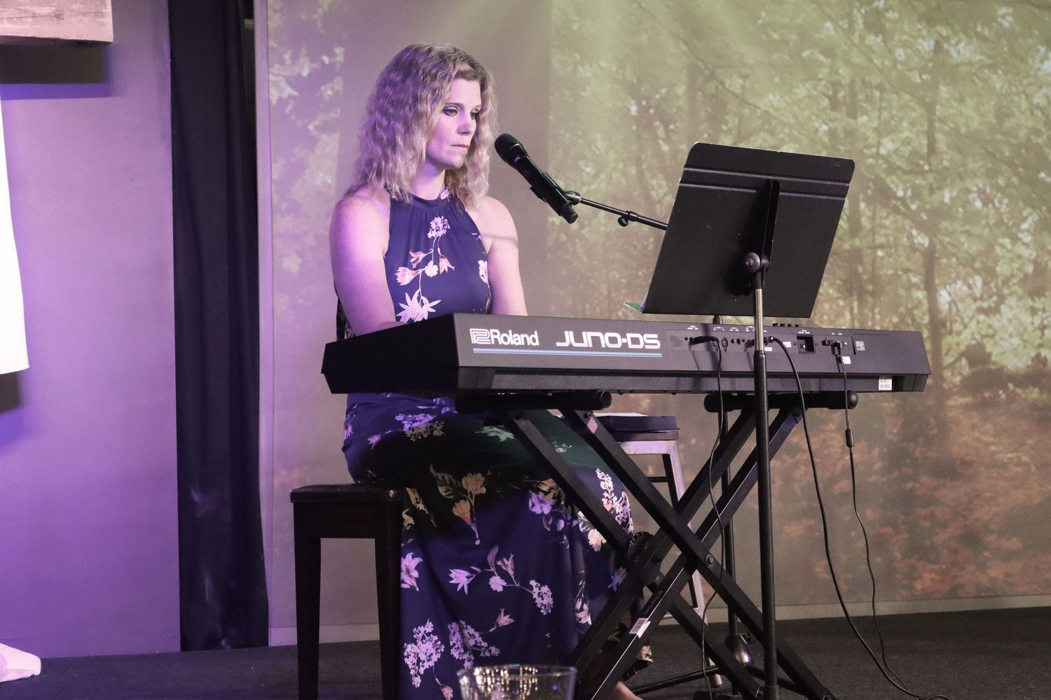 Musician performing on keyboard at venue with purple lighting and textured background.