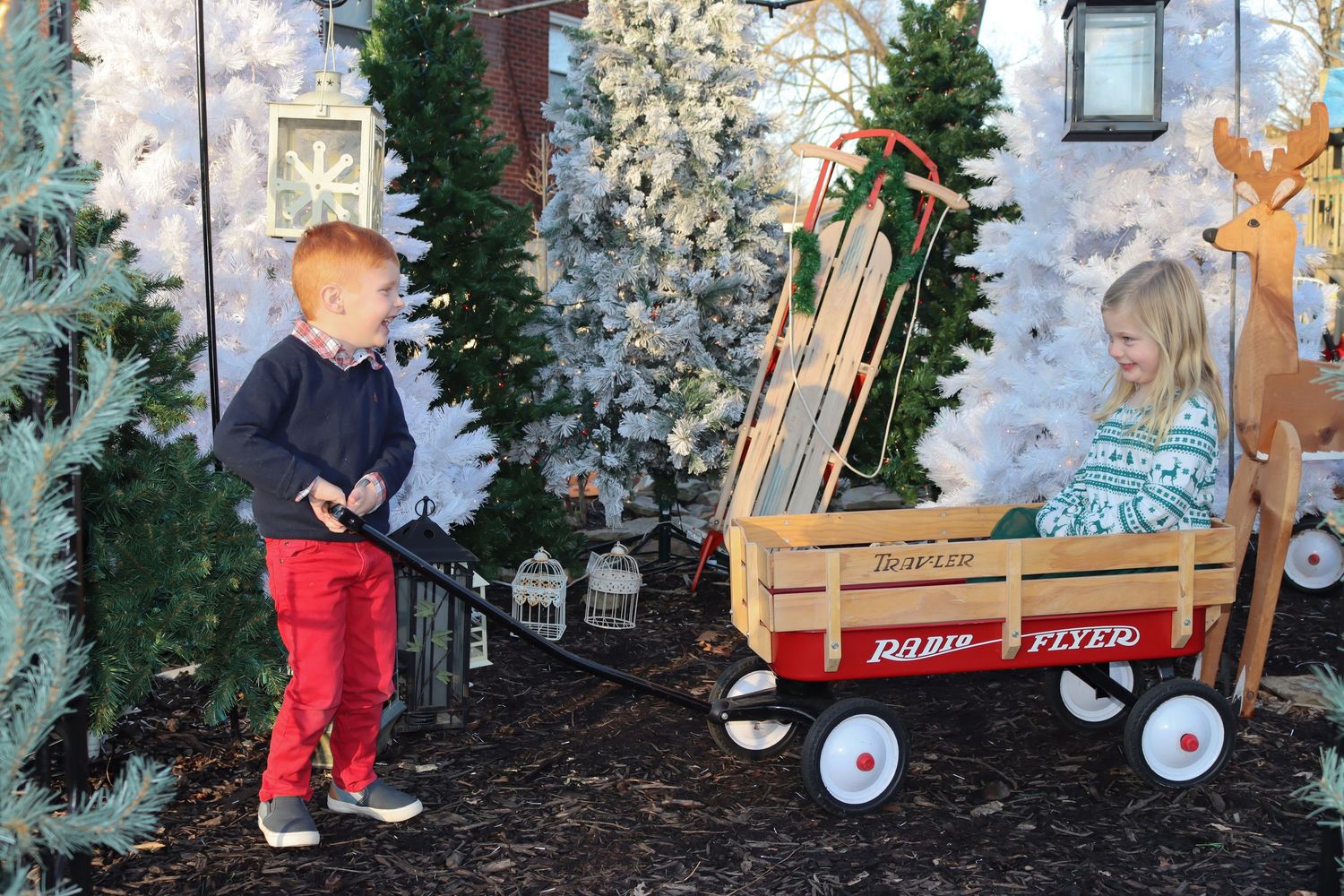 Children play near decorated Christmas trees with a classic Radio Flyer wagon.