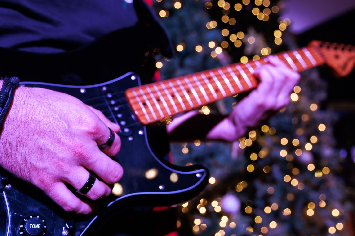 Electric guitar strings being played against a backdrop of blurred holiday lights.