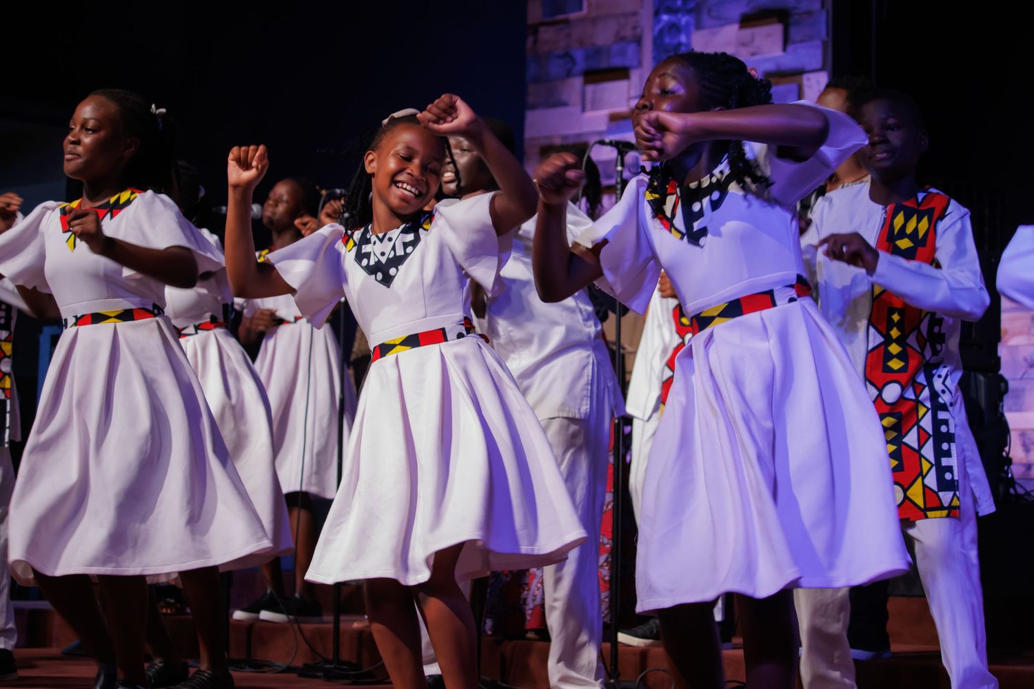 Gospel choir performers in white dresses singing passionately during a stage performance.
