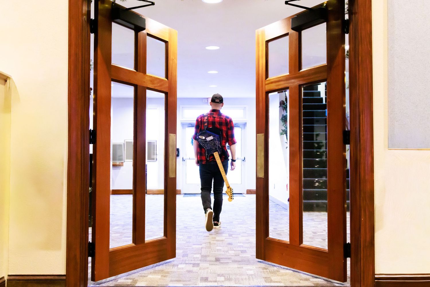 A person in red walking away through large wooden double doors in a bright hallway.