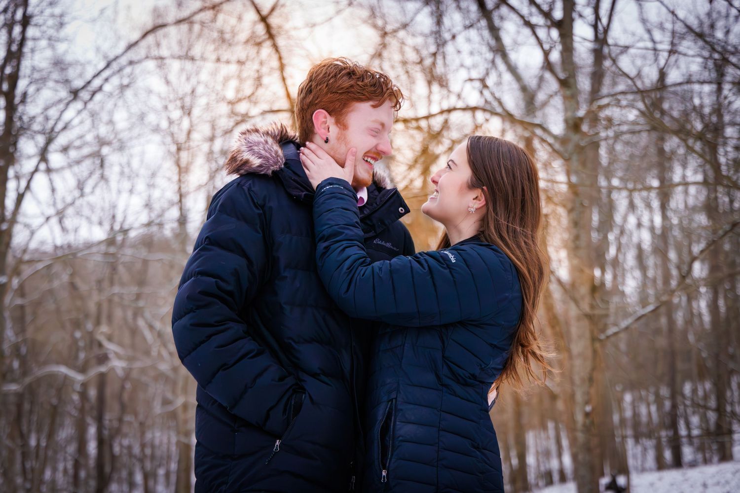 A romantic winter scene shows a couple embracing in a snowy wooded area.