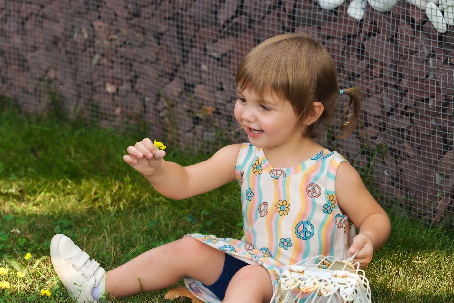 Child sitting on grass wearing colorful peace sign dress.