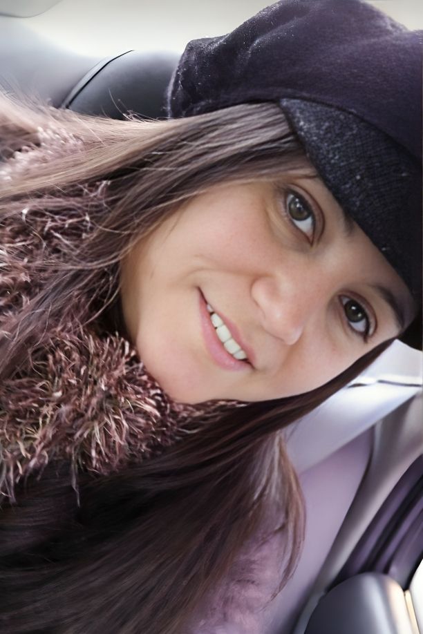 Close-up selfie showing long brown hair and a black hat taken from inside a car.