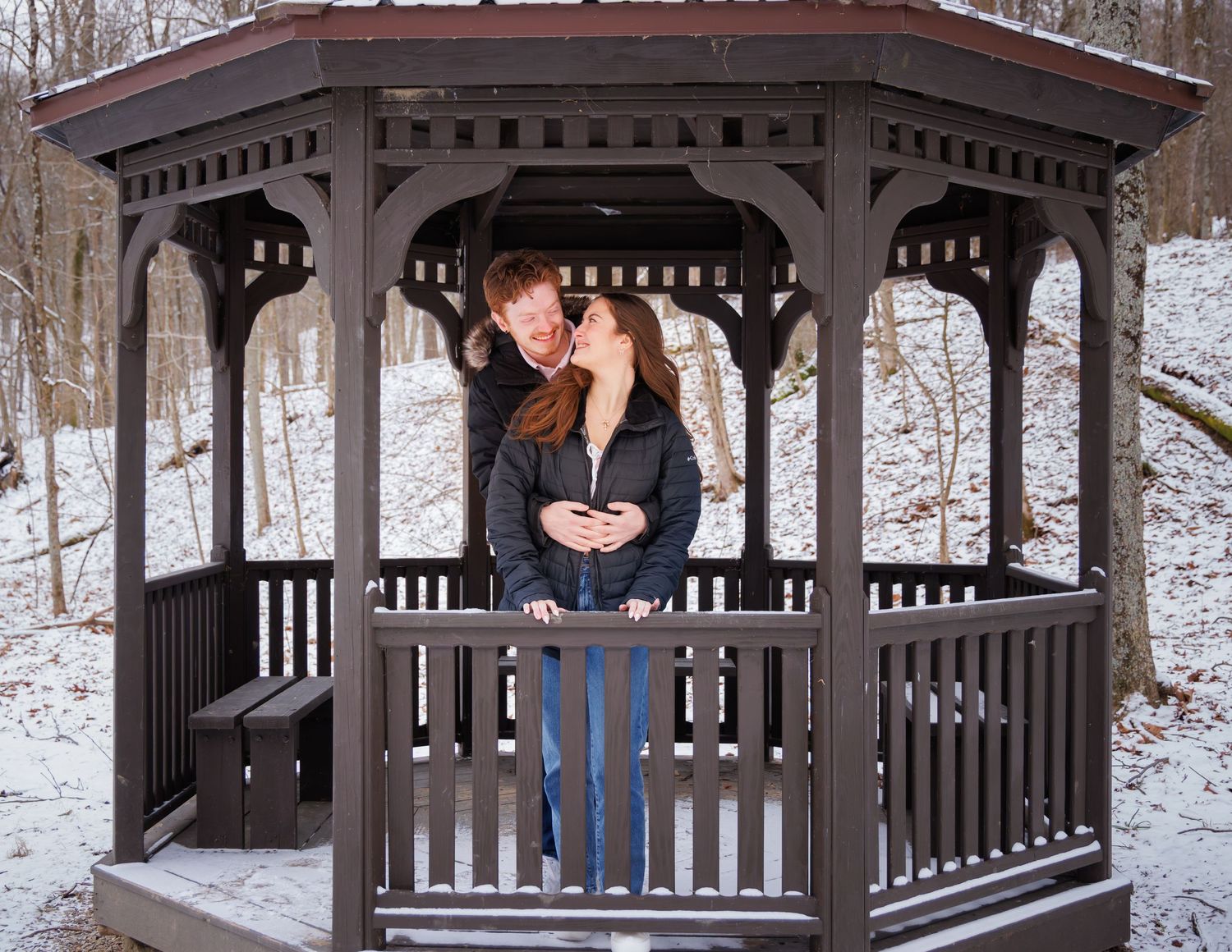 Snow-covered wooden gazebo in winter forest setting.