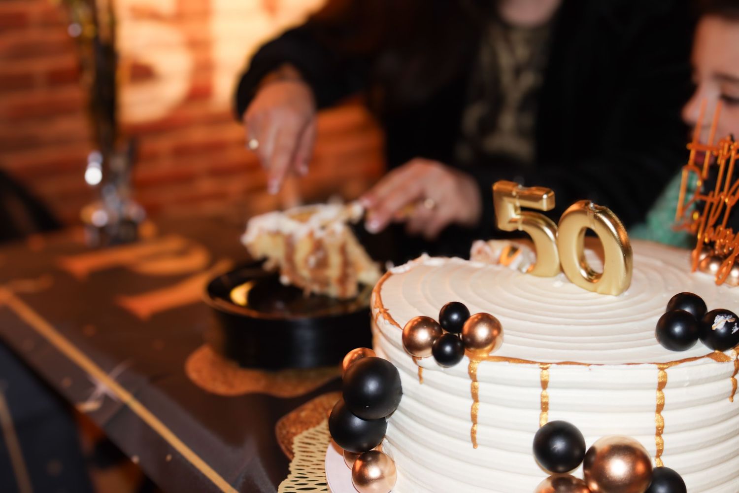An elegant white 50th anniversary cake decorated with black and gold spheres and metallic accents.