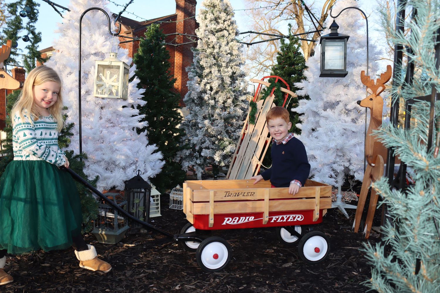 A vintage red wagon sits among decorated Christmas trees and snowy winter scenery.