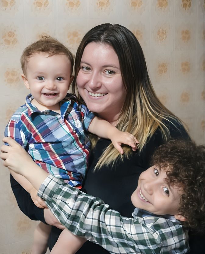 Candid family photo showing playful interaction between parent and children against floral wallpaper.