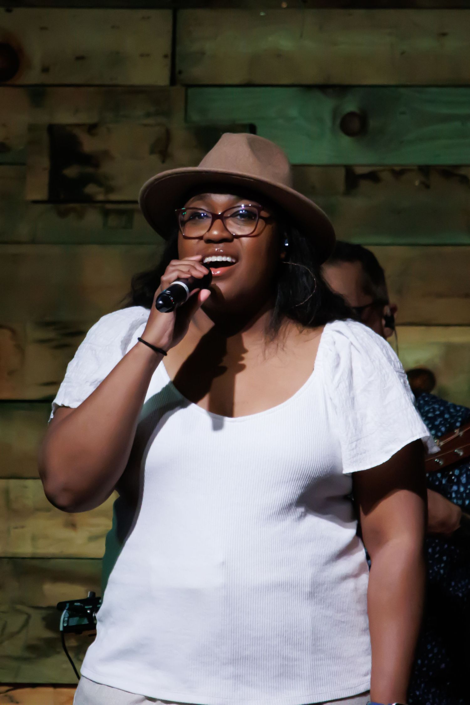 Singer in a white top performing on stage with expressive gestures.