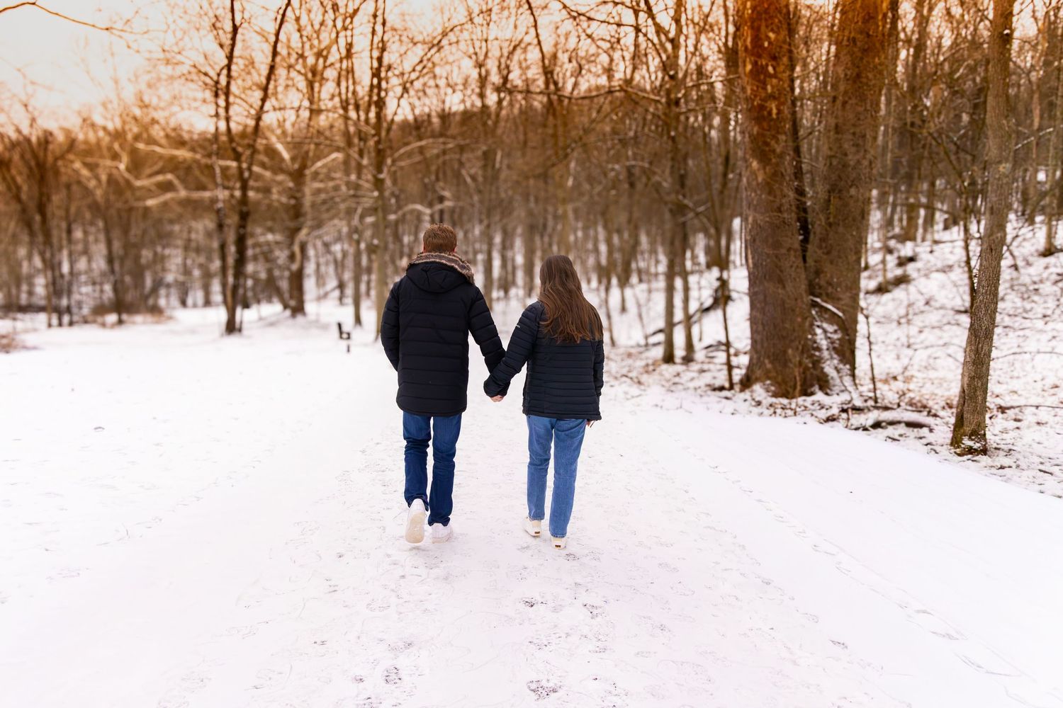 People walking through a snowy forest path during winter sunset.