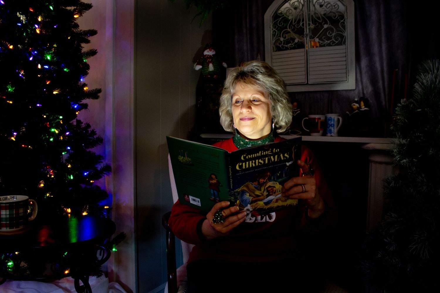 A person reading a Christmas book by the glow of holiday lights near a decorated tree.