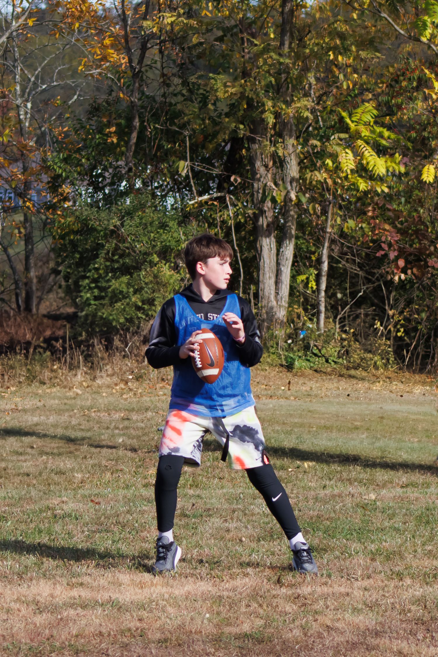 A player in blue jersey practicing football moves on an autumn field.