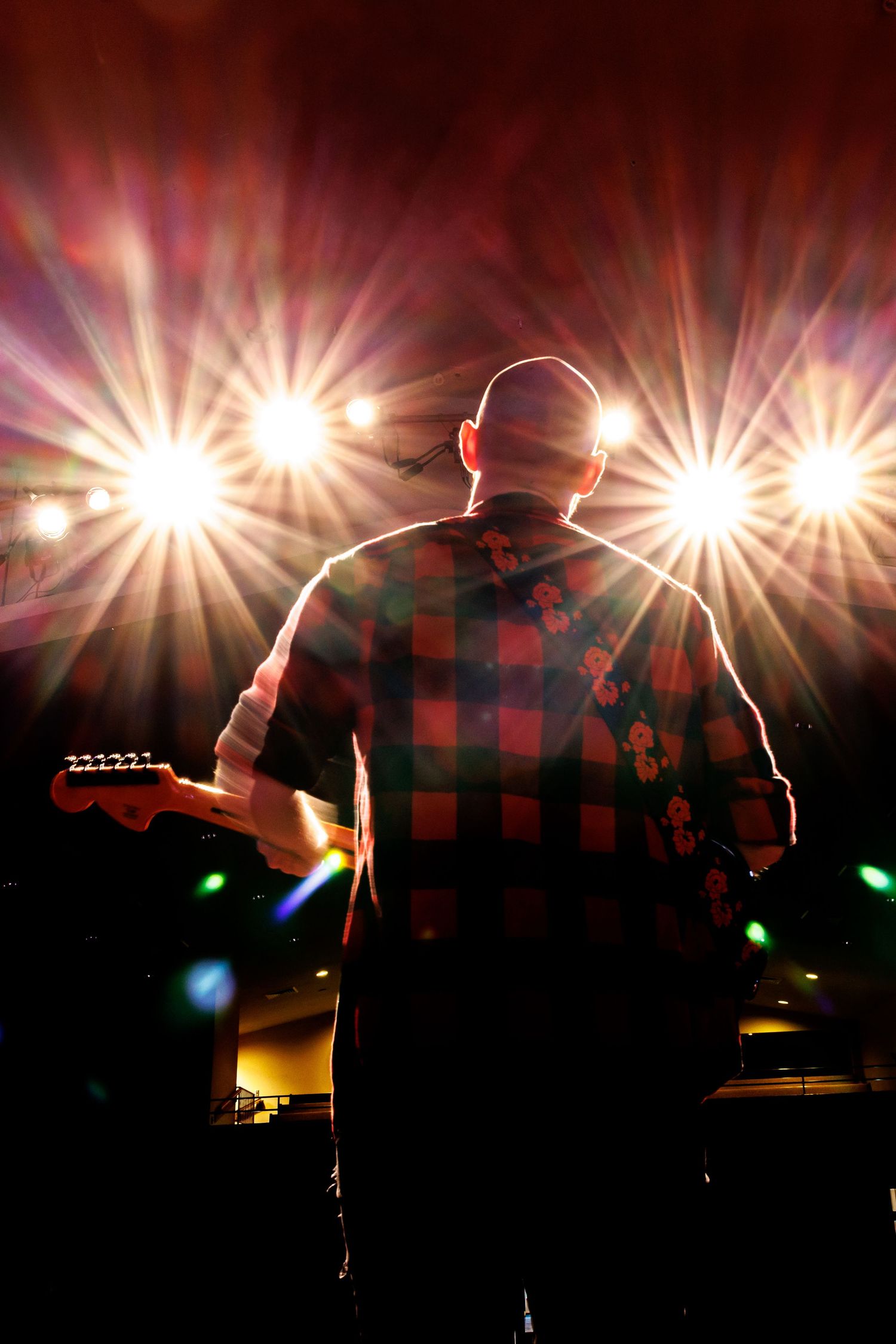 Silhouette of guitarist performing on stage with bright starburst lights behind them.