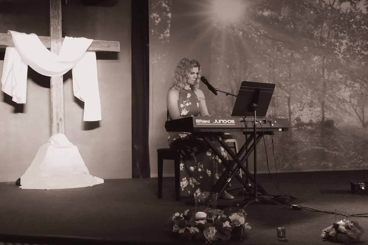 Black and white photo of a performer playing keyboard on stage with decorative backdrop.