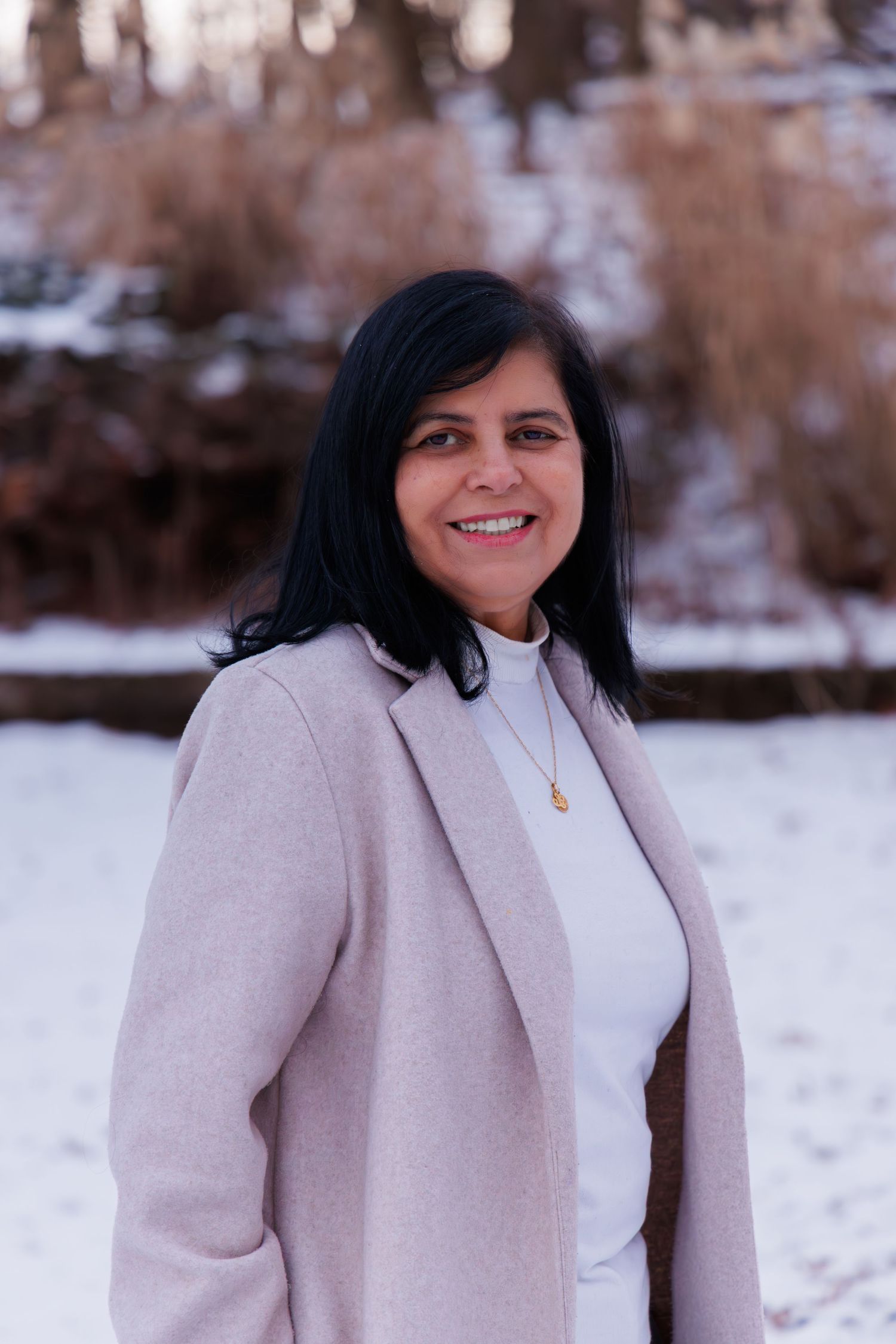 Person wearing a light beige coat poses in a snowy winter setting.