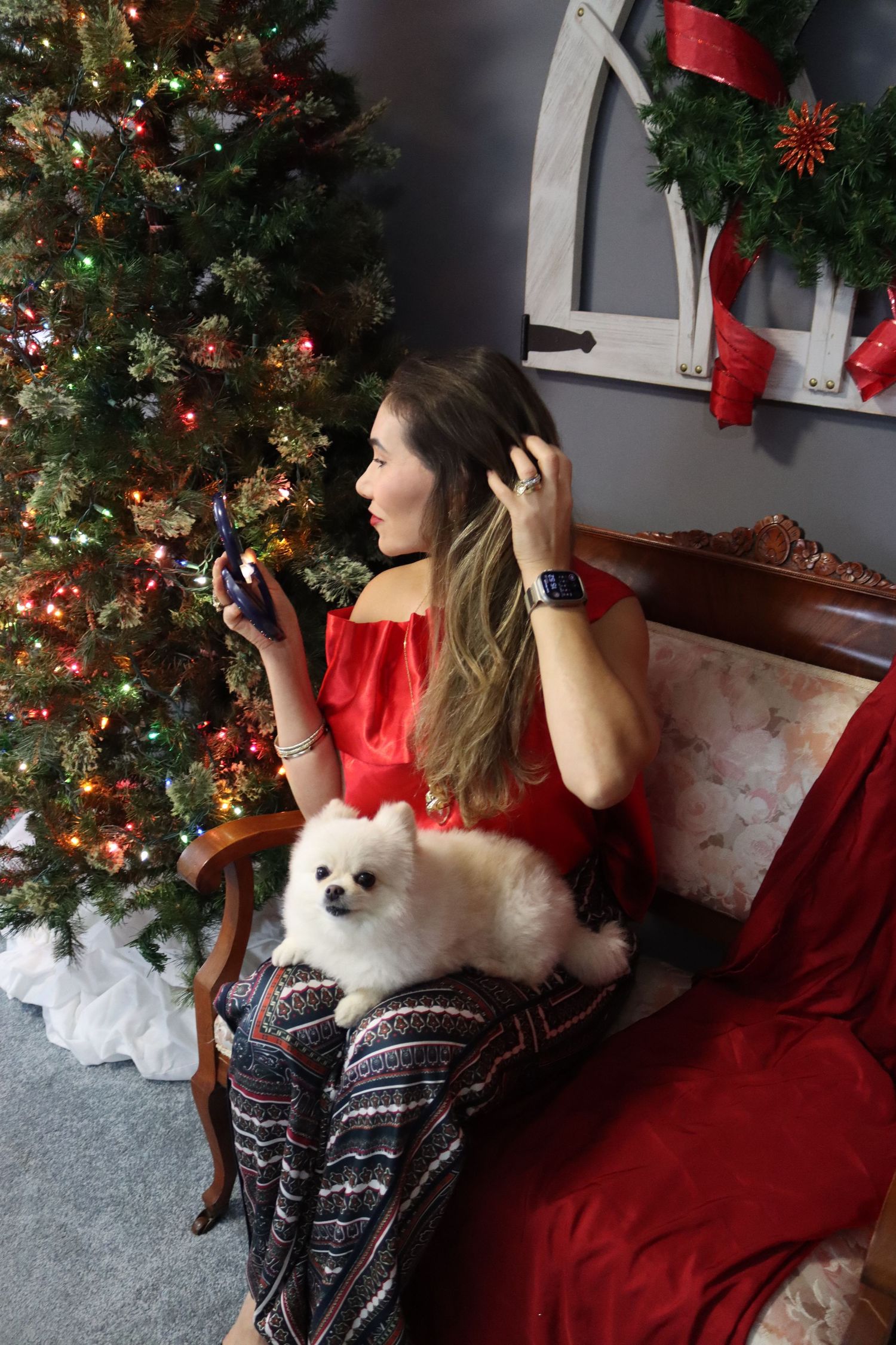 White Pomeranian dog sitting on red couch with Christmas tree in background.