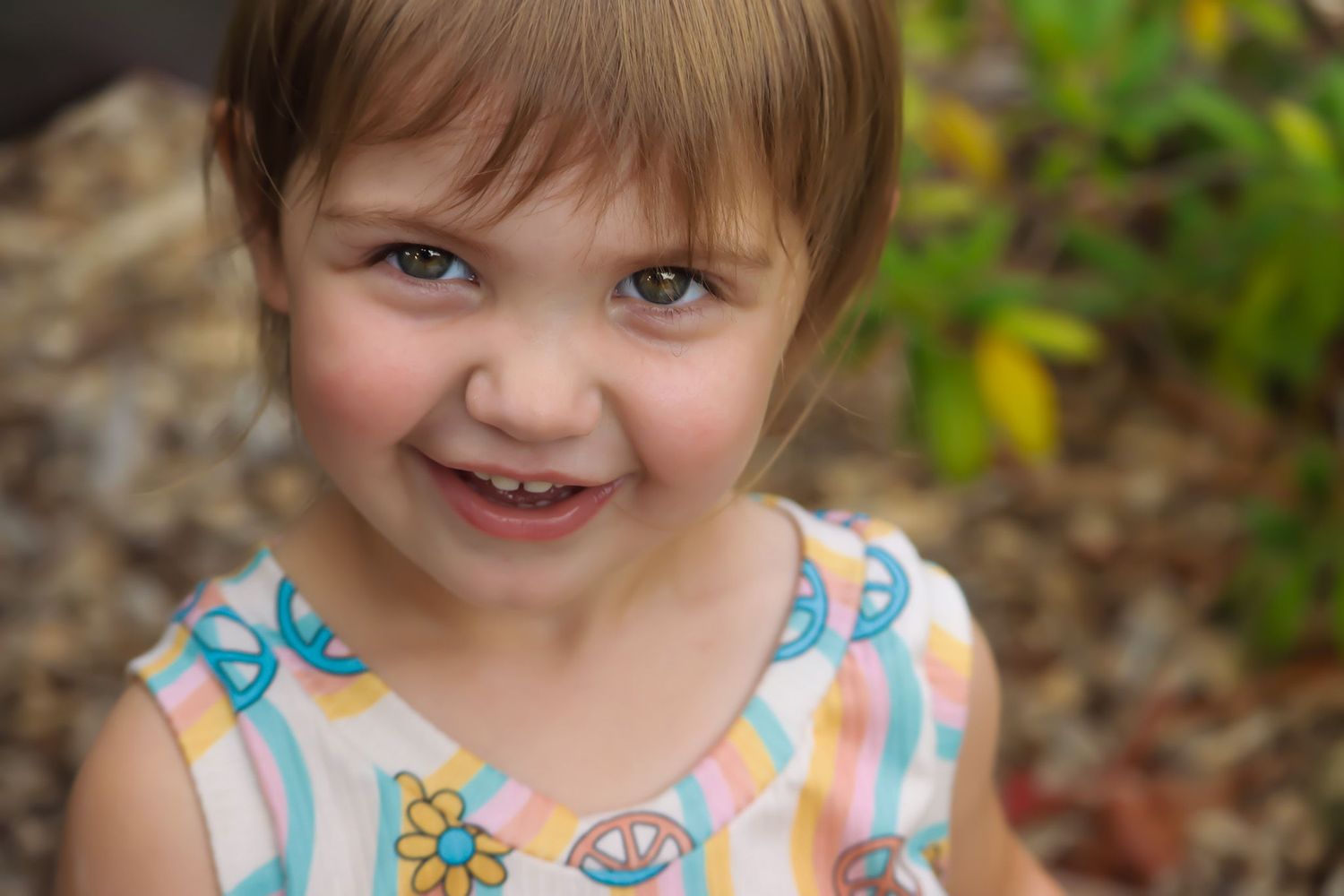 Portrait of a young child in floral dress smiling outdoors.