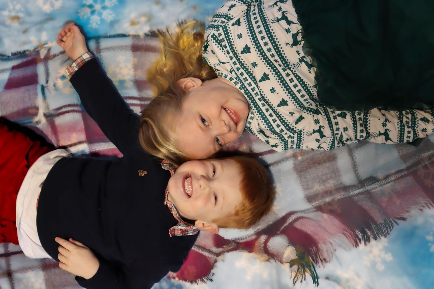 Two children laying down and laughing during a winter holiday photoshoot.