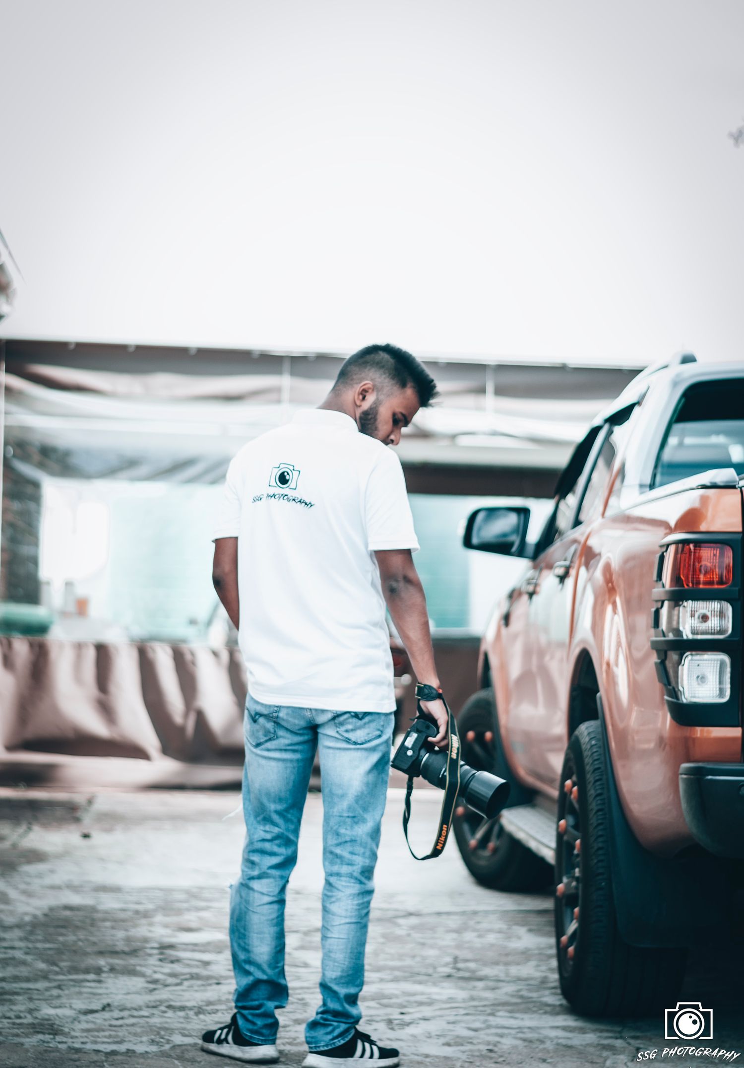 Close-up view of person in jeans and white t-shirt standing next to cars in a parking lot.