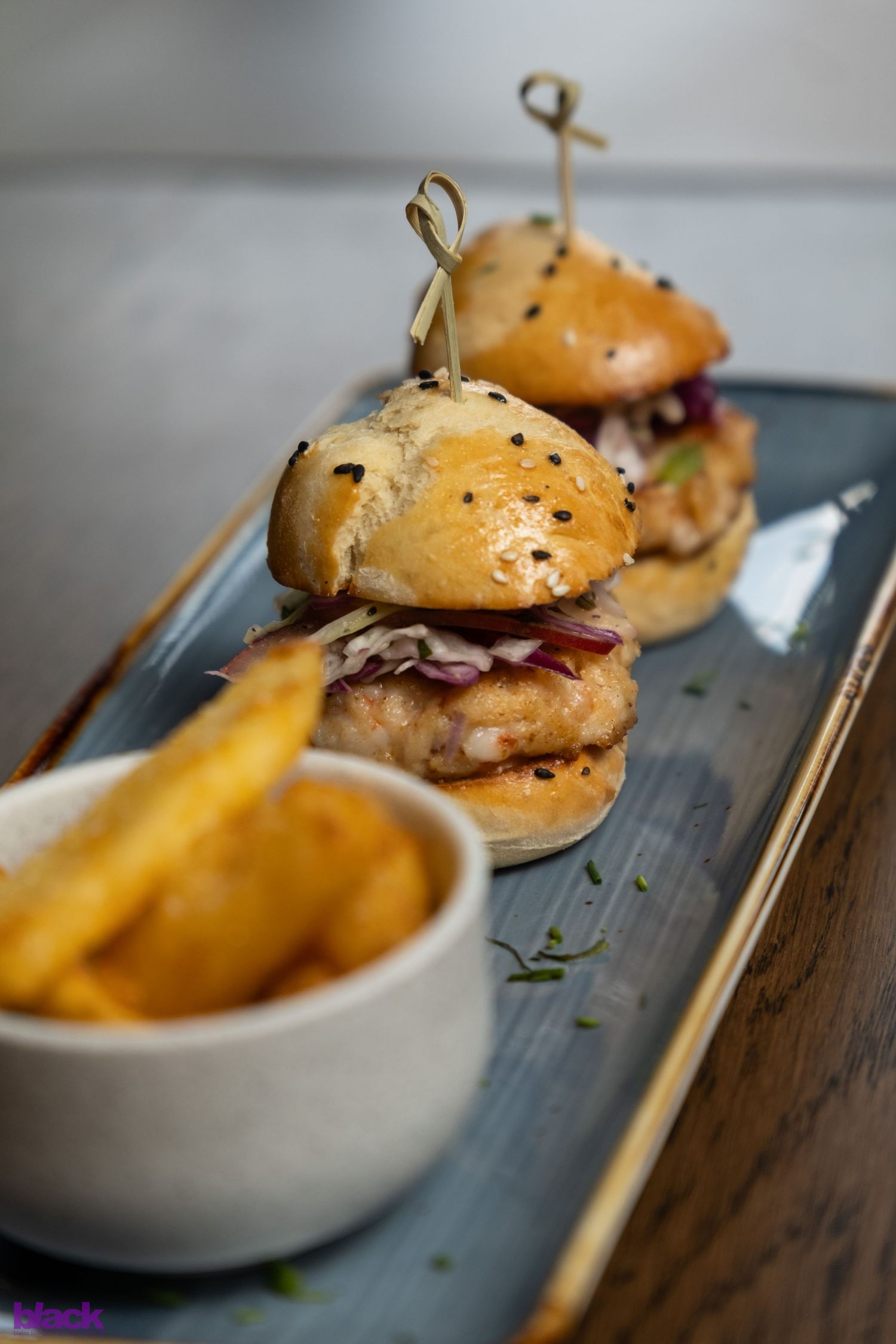 Mini sliders with french fries served on a dark slate platter with garnish.