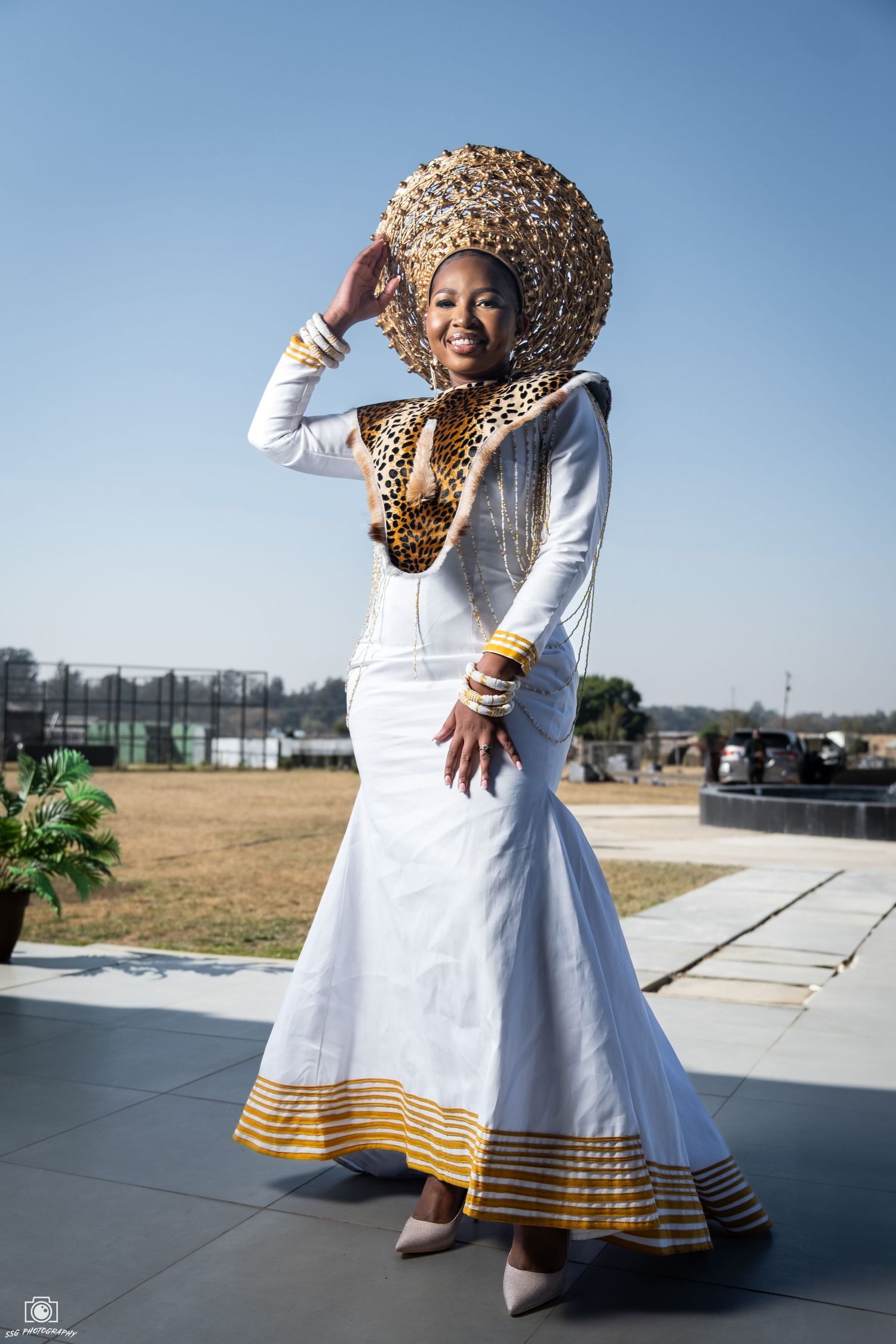Dancing poses in a white traditional dress with gold trim against a blue sky background.