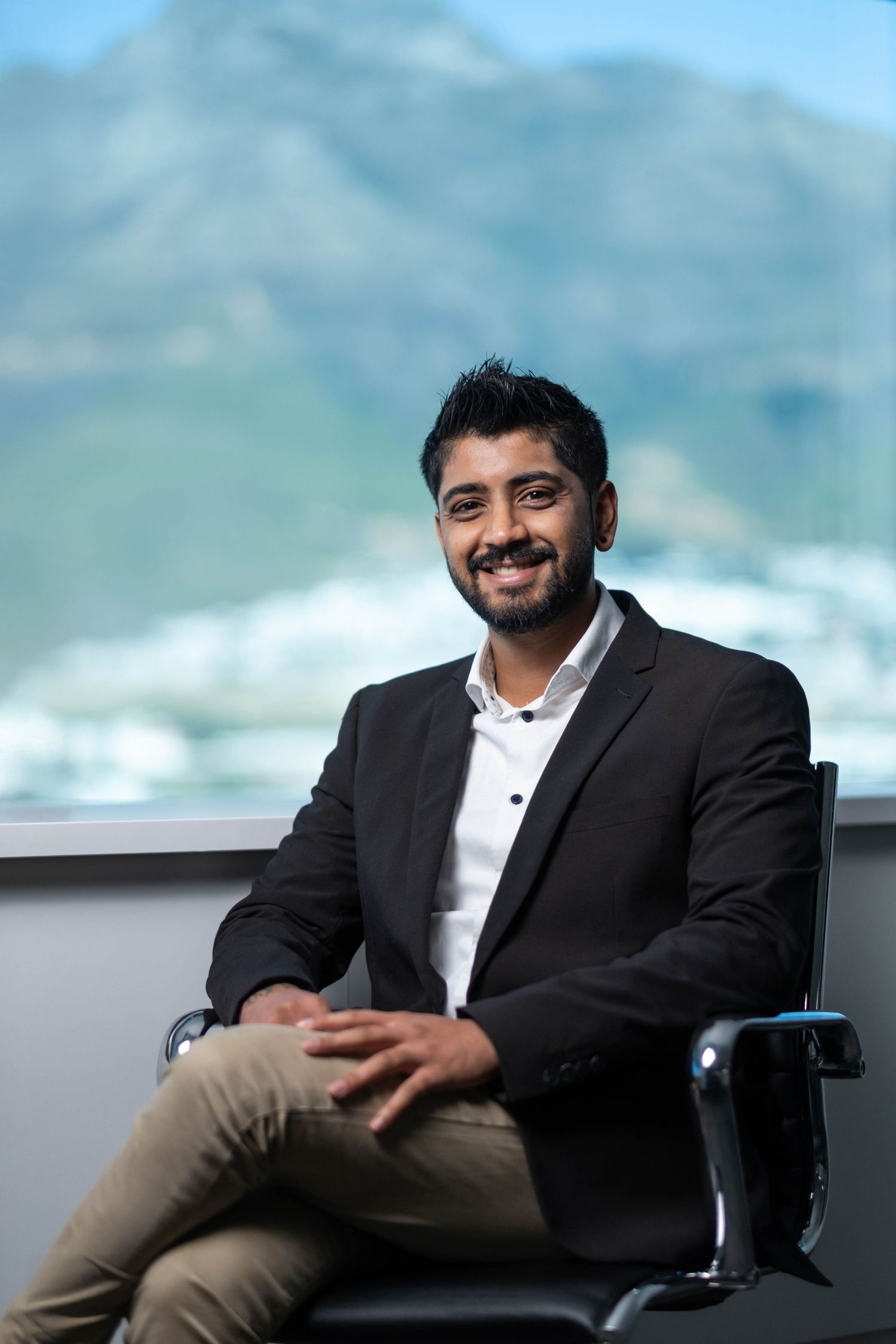 Business professional in suit seated in modern office with mountain scenery.