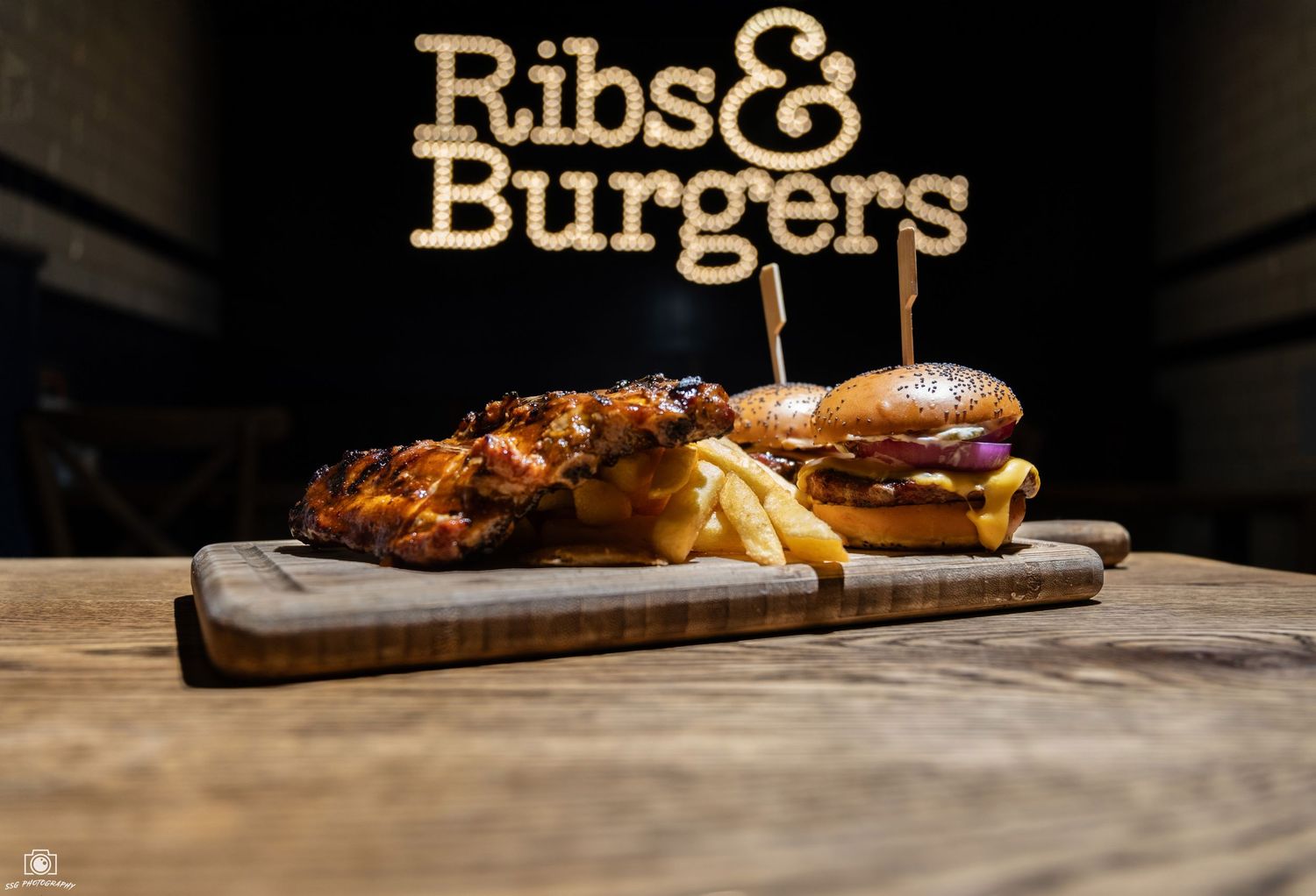 Wooden restaurant tables with Ribs & Burgers signage visible in background.