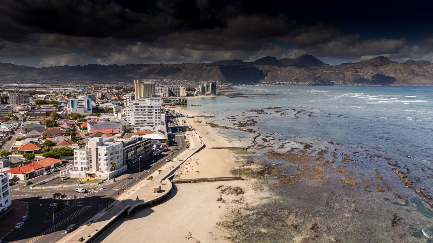 Wide panoramic view of a coastal city with buildings and beach stretching along the shoreline.