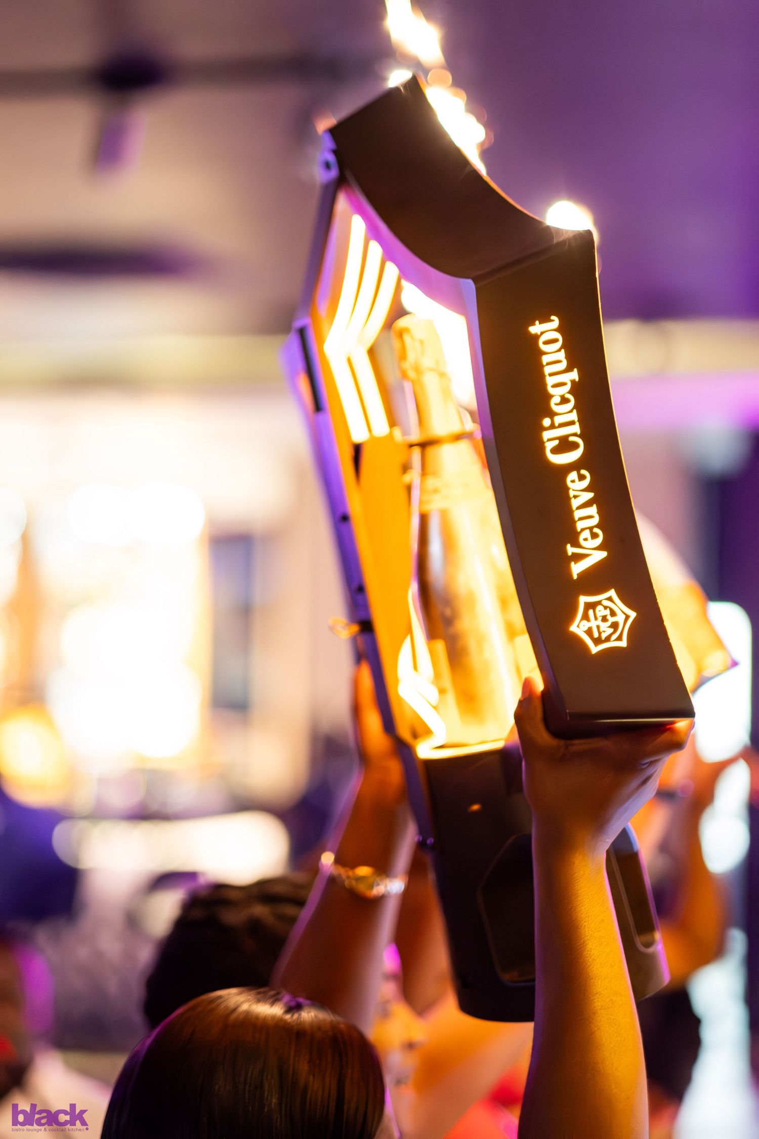 Illuminated bottles raised in celebration against purple party lighting.