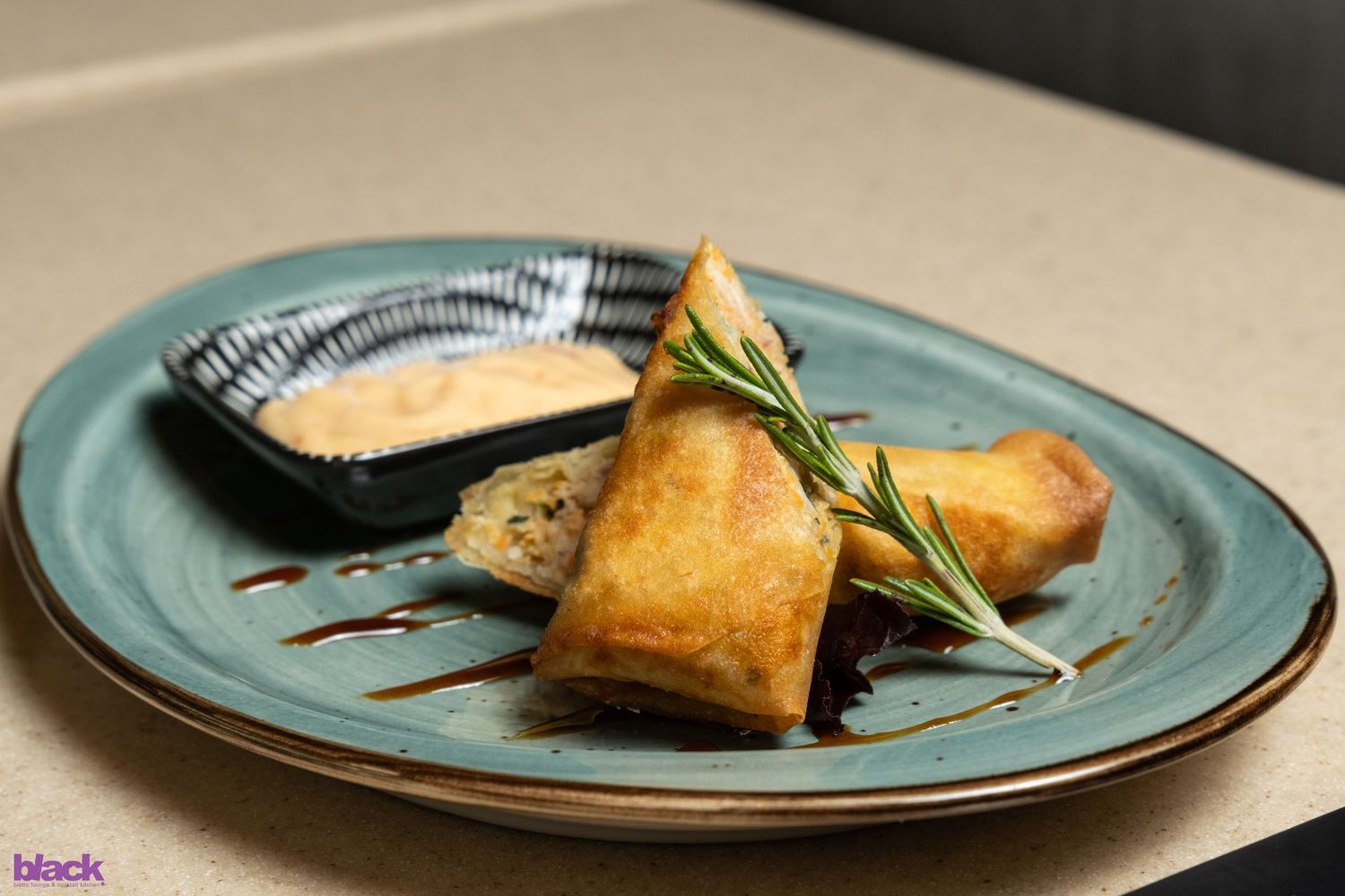 Golden fried spring rolls served on teal plate with dipping sauce and fresh herbs.