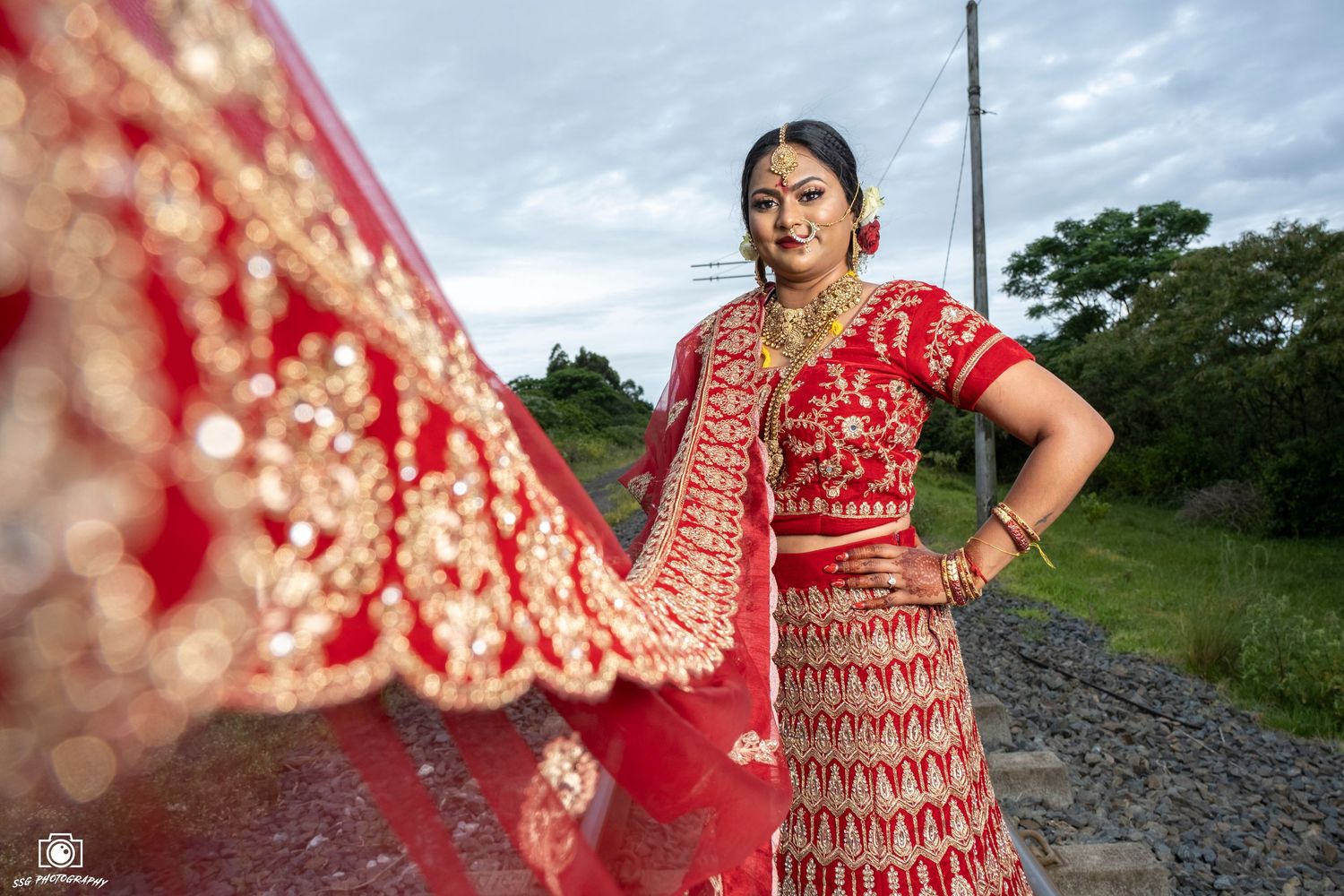 Traditional red and gold embroidered lehenga captured against a cloudy sky.