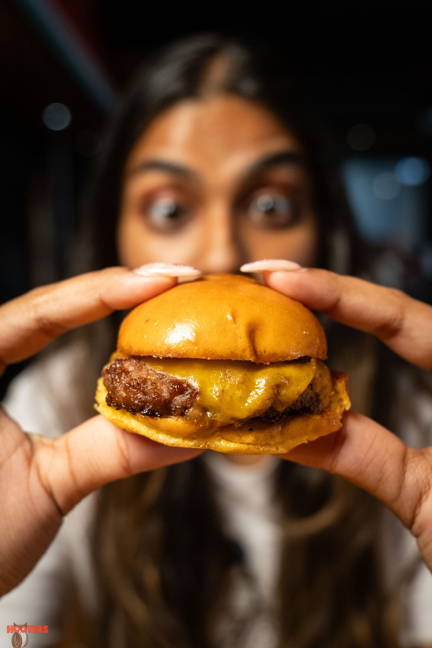 Hands holding a juicy cheeseburger with melted cheese against dark background.