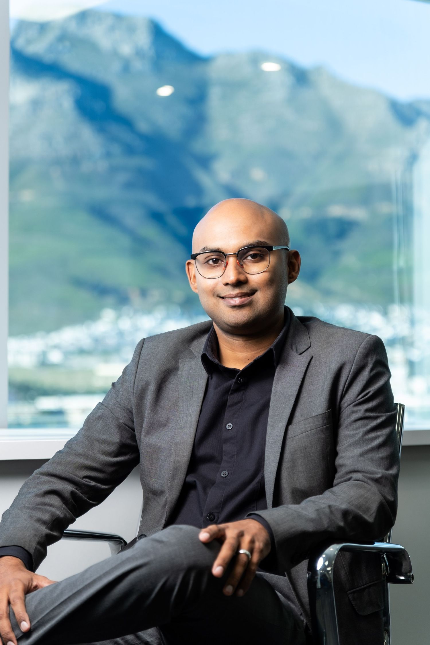 Professional in business attire seated in office with mountain view background.